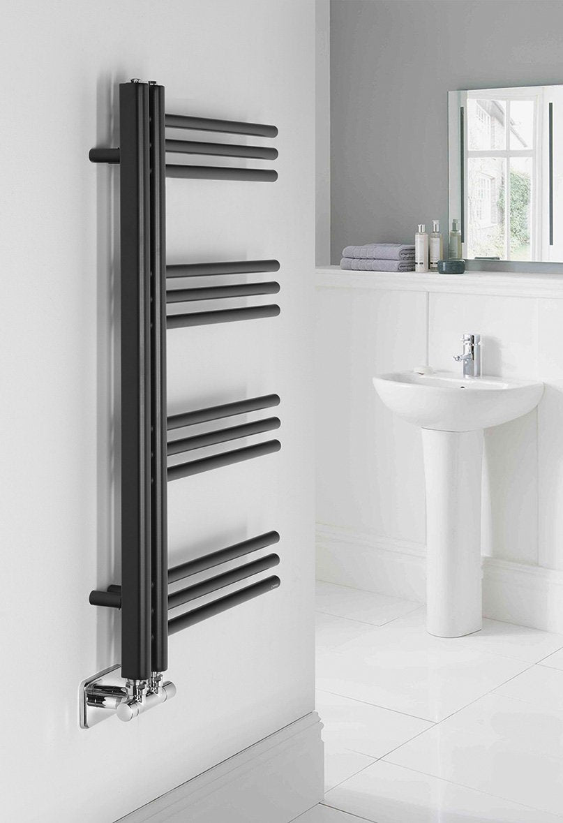 Kopalniški radiator SAPHO DORLION, 500 × 900 mm, mat črn – izdelek 1130-20 – primer postavitve v prostoru. Na sliki so prikazani tudi priključni ventili; vsebina nakupa je navedena v opisu. Pohištvo in oprema prostora nista vključena v nakup.